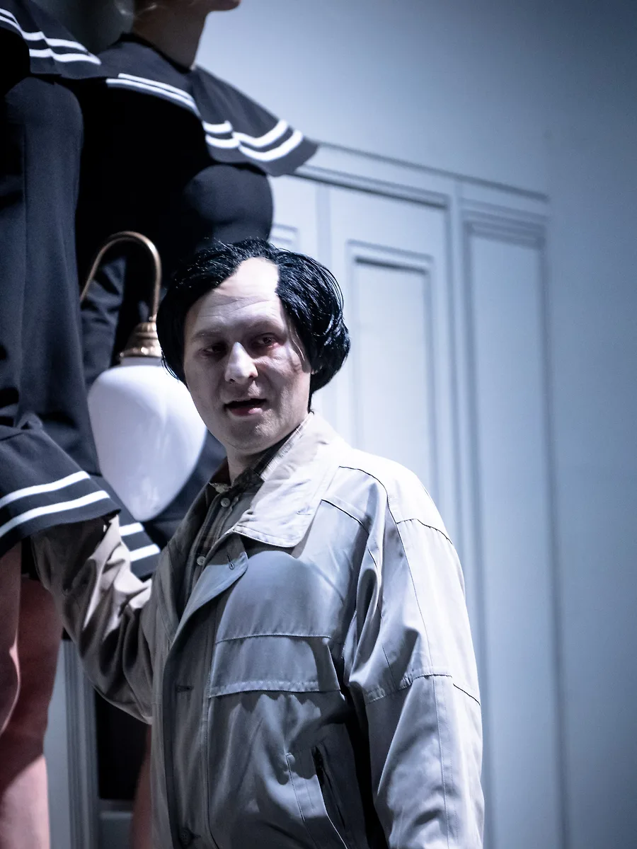 Semjon Bulinsky als Delbert Grady in Moravecs „The Shining“, schwarze Perücke und weiß geschminktes Gesicht, unter einer Wandlampe, hinter ihm die Zwillinge in gestreiften Kleidern