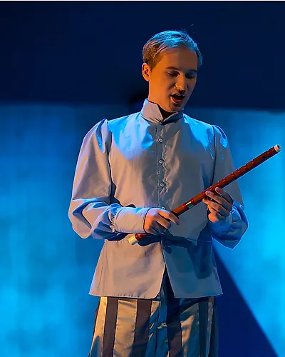 Semjon Bulinsky als Tamino, die Flöte in beiden Händen, vor blauem Bühnenlicht