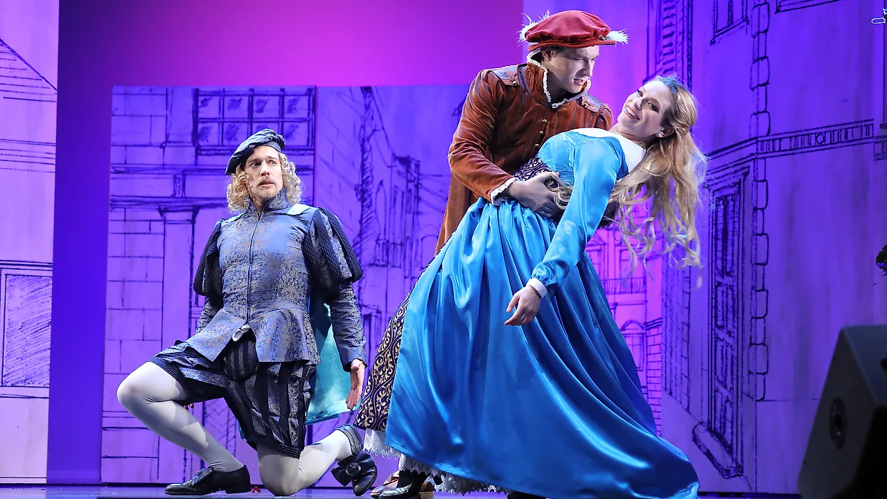 Semjon Bulinsky als Bill Calhoun in Porters „Kiss Me, Kate“, im roten Wams mit Federhut, seine Partnerin im blauen Kleid in einer Hebefigur