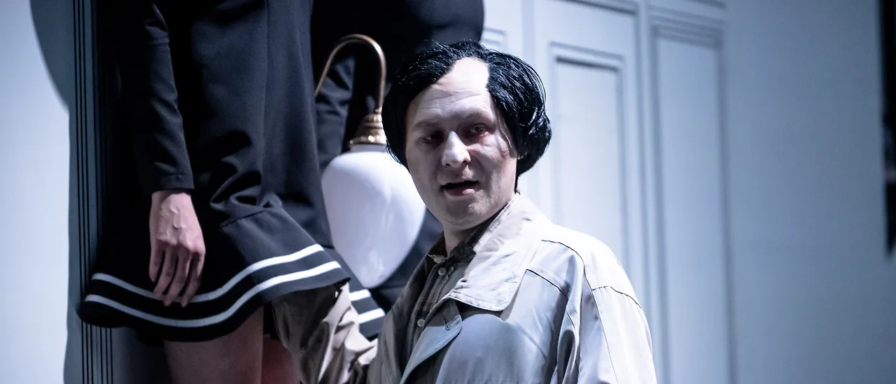 Semjon Bulinsky als Delbert Grady in Moravecs „The Shining“, schwarze Perücke und weiß geschminktes Gesicht, unter einer Wandlampe, hinter ihm die Zwillinge in gestreiften Kleidern